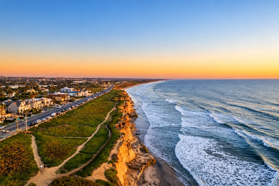 Aerial view of coastal bluffs, a seaside road and Pacific waves in warm evening light